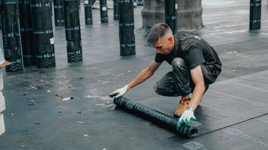 Construction worker applies waterproof membrane on rooftop for protection against weather elements.